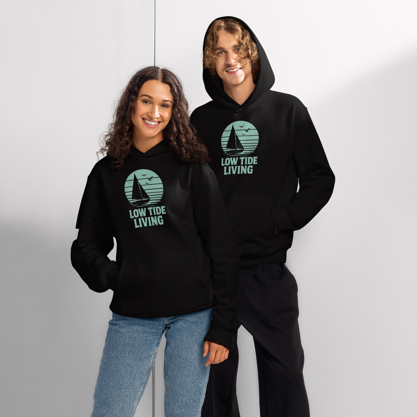 Solstik two models wearing black premium heavyweight pullover hoodie with teal Low Tide Living sailboat logo