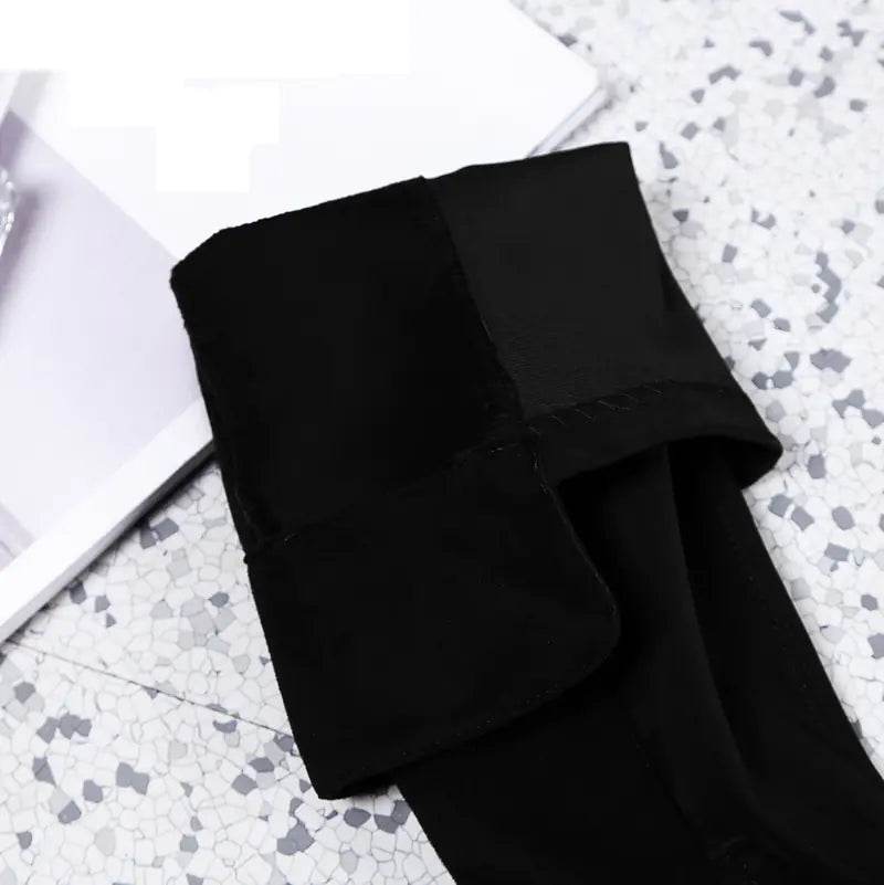 Black velvet stretch thigh high boots folded on marble tile floor next to a white book