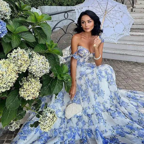 Woman wearing a blue floral off-shoulder evening gown holding a white lace parasol outdoors