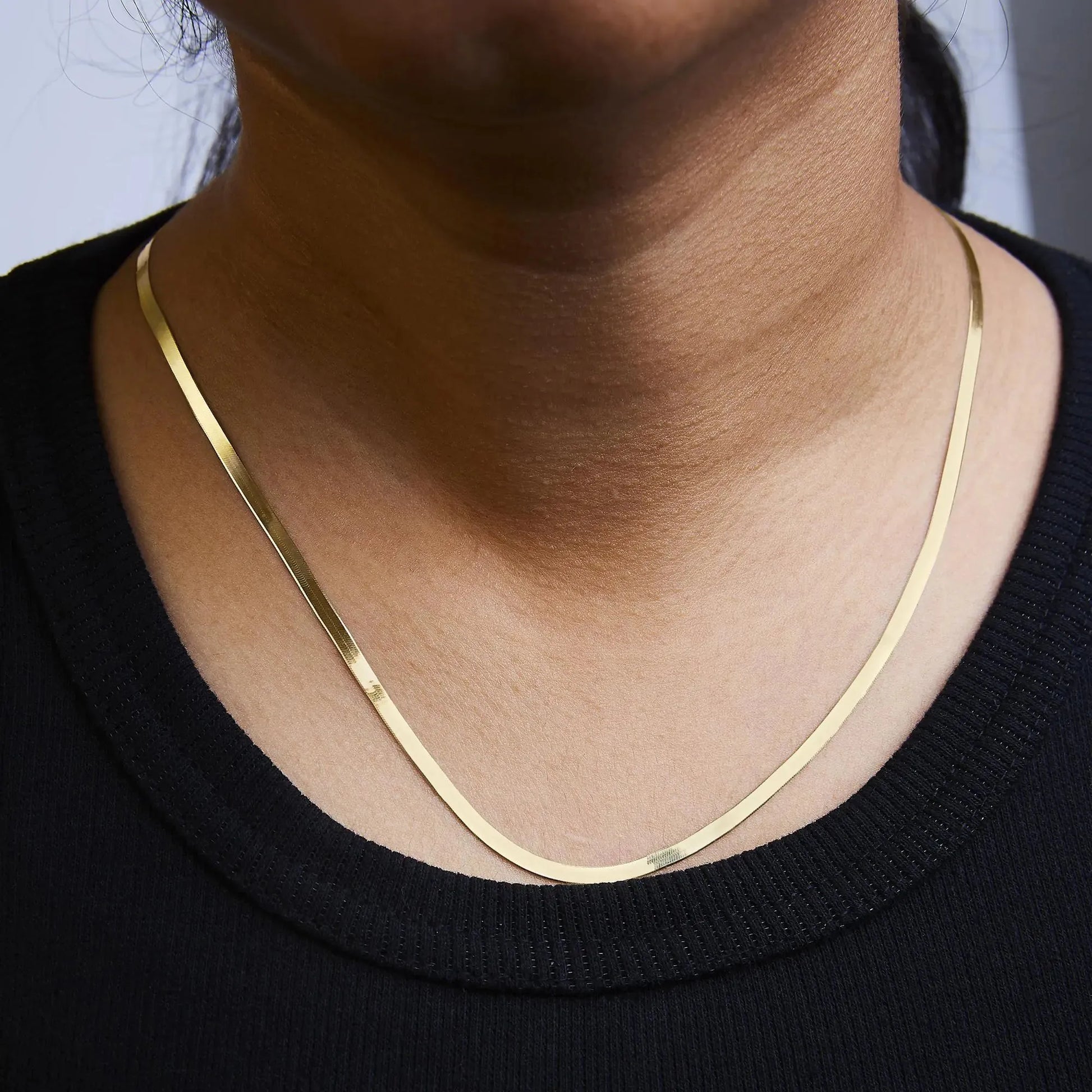 14k gold herringbone chain necklace worn on neck with a black top background