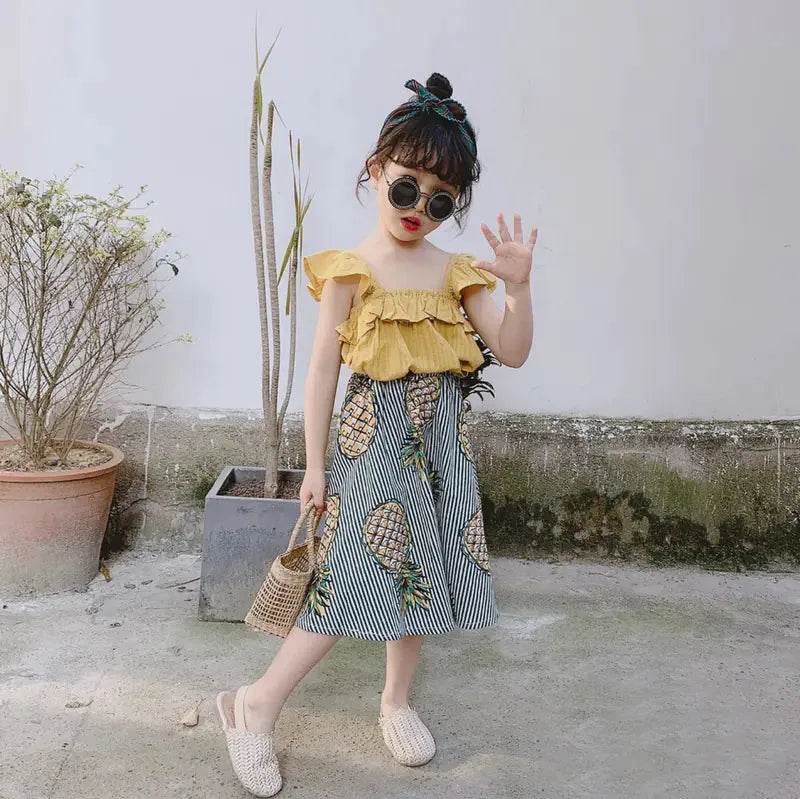 Girl wearing girls pineapple skirt and top set with yellow ruffled top and striped skirt with pineapple print