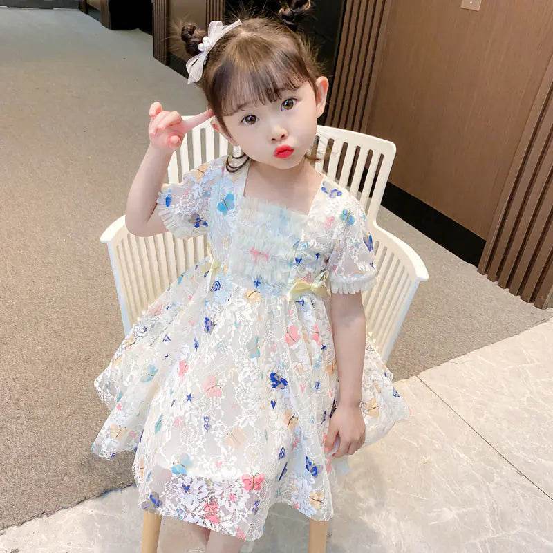 Little girl wearing a colorful girls summer lace gown sitting on a white chair indoors