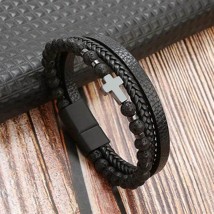 Solstik men's braided leather wristband with black beads and silver cross charm on wooden surface