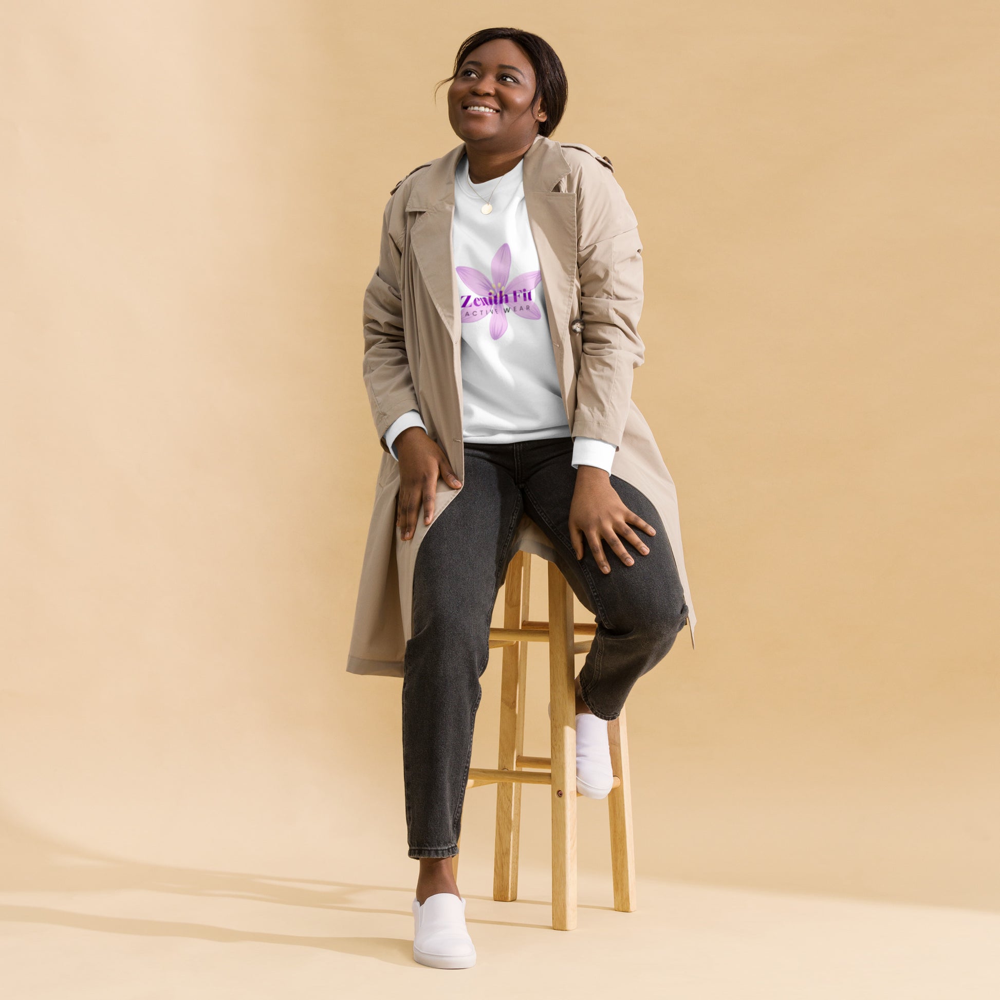 Solstik exclusive fleece crewneck worn under a beige trench coat on a smiling model seated on a wooden stool