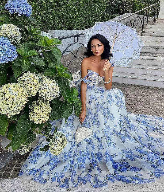 Woman wearing a blue and white floral off-shoulder evening gown holding a lace parasol outdoors