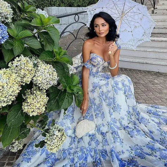 Woman wearing a blue floral off-shoulder evening gown holding a white lace parasol outdoors