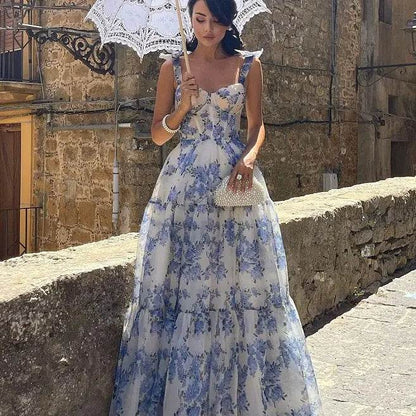 Solstik off-shoulder evening gown with blue floral pattern worn with a white umbrella and clutch